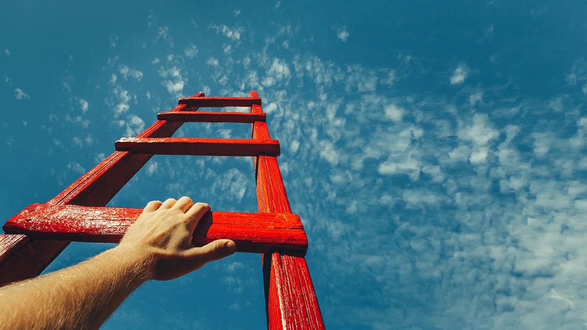A man's hand on a red ladder that's going up into the bright blue sky